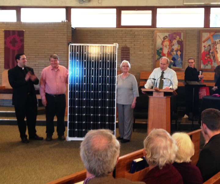 A solar panel is displayed as parishioners hear the project announcement.   Left to right:  Fr. Pat Cahill, Care of Creation members:  Bruce Cahoon, Joyce Drapeau and Bill Maloney