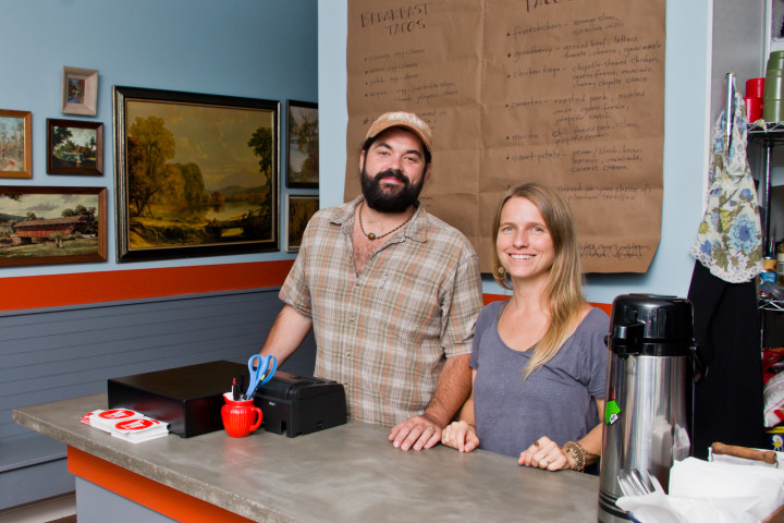 GOAT ART: The interior of TacoBilly's space at 201 Haywood Road features a collection of old paintings, each accented with the restaurant's signature orange billy goat. Pictured are owners Hunter and Beth Berry.  Photo by Cindy Kunst