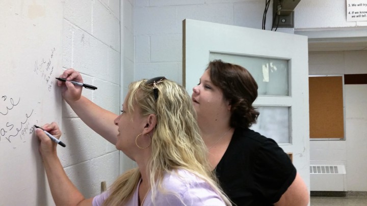 Connie Carland and Marie Vaughan, class of 1994, sign the wall of their old math classroom at Asheville Middle School