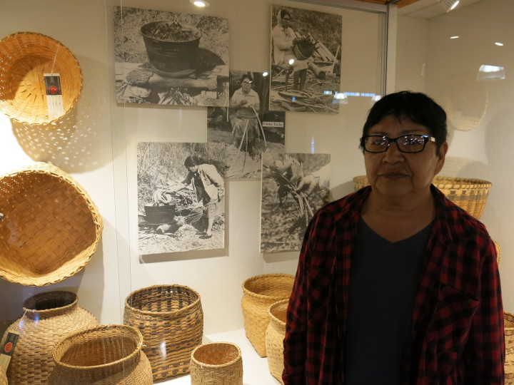  CARRYING ON TRADITION: Basketmaker Faye Junaluska stands before her mother's works, on display inside the Permanent Collection Gallery of the Qualla Arts and Crafts Mutual, Inc. Photo by Thomas Calder 