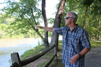 MAKING WAVES: Marc Hunt gestures to the calm waters that flow beside Woodfin River Park, pointing out the future location of the Asheville area’s first constructed whitewater wave. Photo by Virginia Daffron
