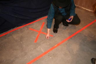 X MARKS THE SPOT? Warren, MacLeod, and the other investigators present strongly believe that the marked area of the AMT basement, above, may be the sight of a rumored tunnel entrance into the building. Here, Warren illustrates the uneven nature of the floor with a tube of chapstick. Photo by Max Hunt