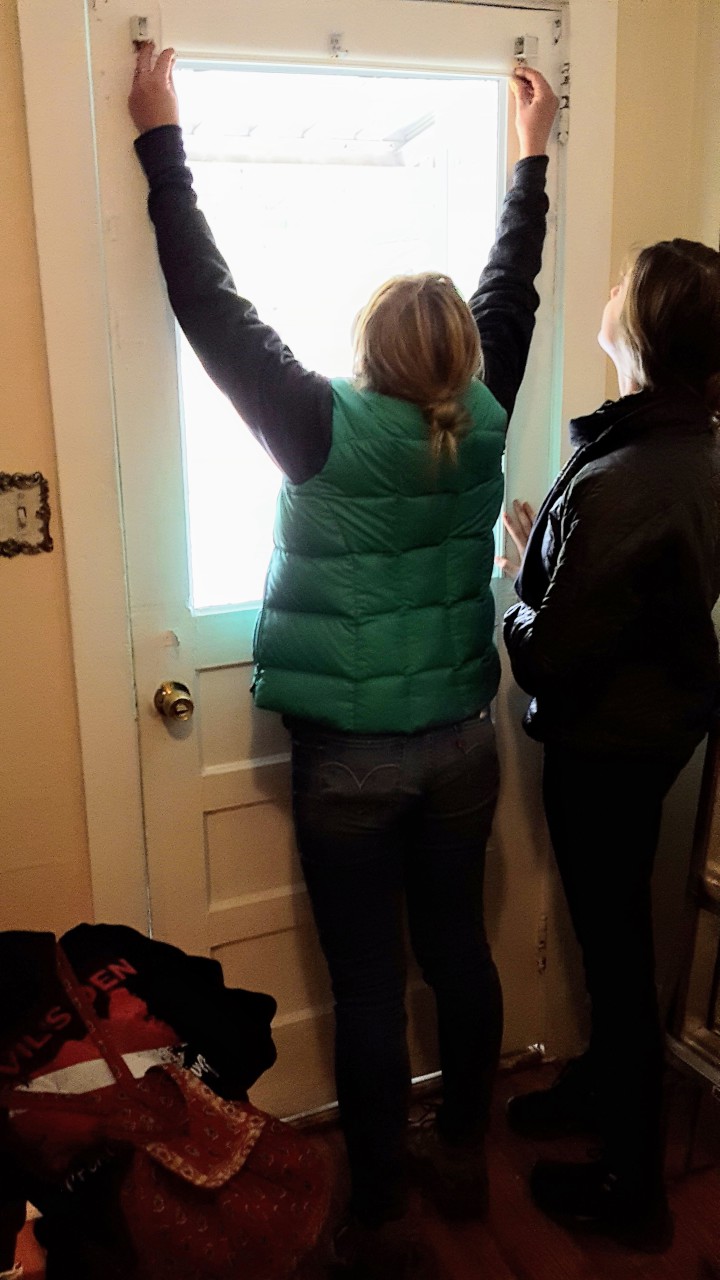 Yulia Shaffer (green vest) of Energy Savers Network with a UNCA volunteer installing an interior storm window on the front door. Photo courtesy of Blue Horizons Project